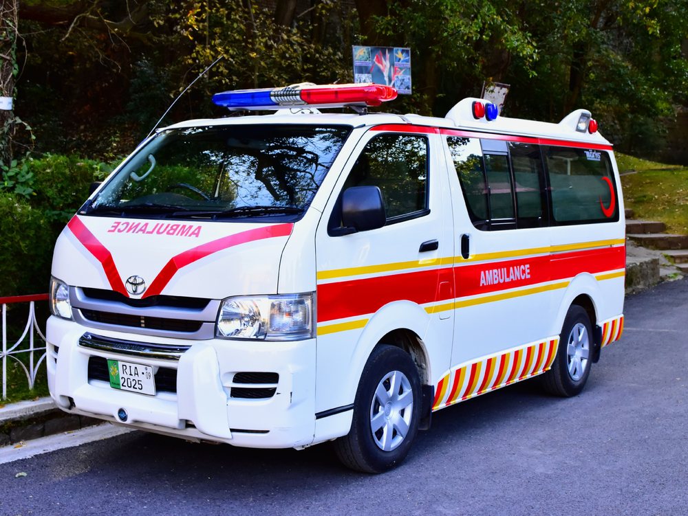 A college ambulance, a white van marked in red and yellow, parked on the campus road