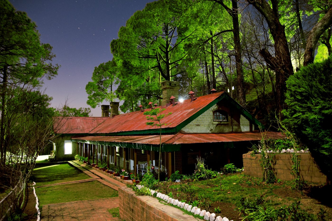 Thurley Hospital at dusk — a long single-storey building with a deep verandah and a corrugated roof, its windows lit, standing among the pines